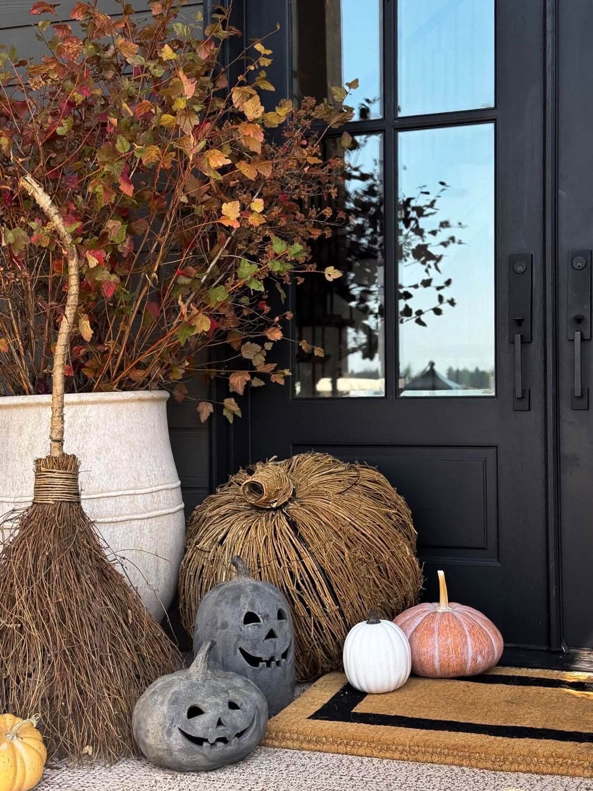 Black front door styled for fall with autumn branches, a twig pumpkin and a broom