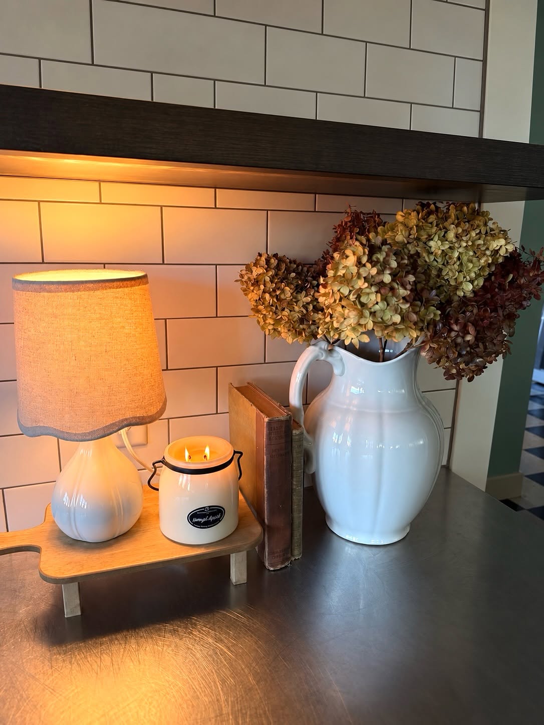 Kitchen counter styled with a scalloped lamp, candle, vintage books and a white pitcher of dried hydrangeas